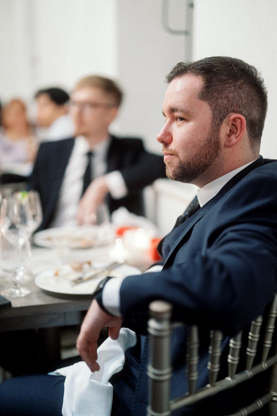 Man in a navy suit seated at a formal dinner table