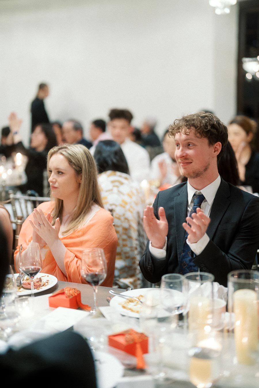 Guests seated at a reception table applauding during a formal dinner.