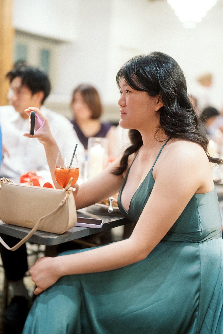 Woman in a green dress seated at a table holding up a phone