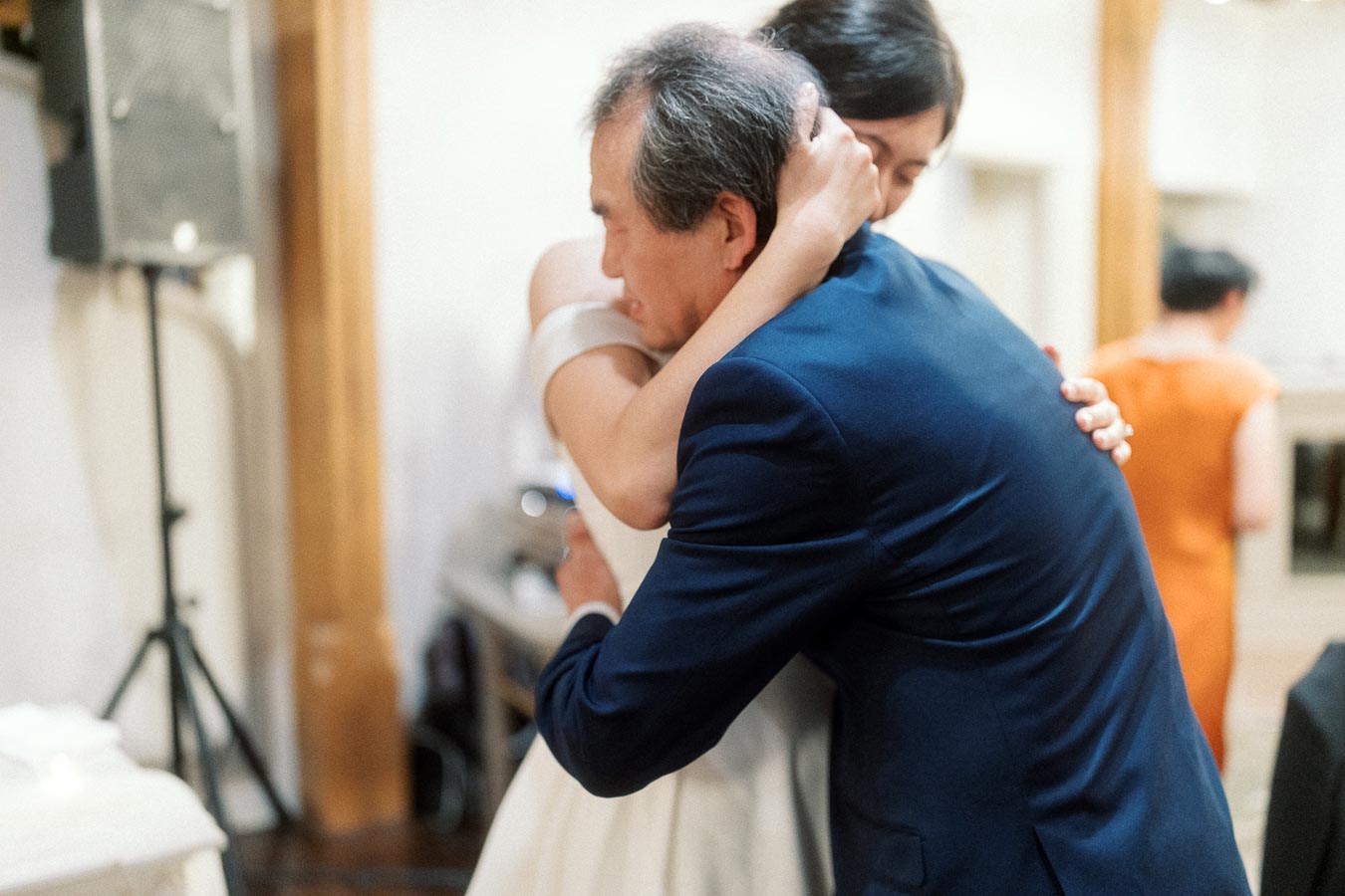 Woman in a white dress embracing a man in a navy suit indoors