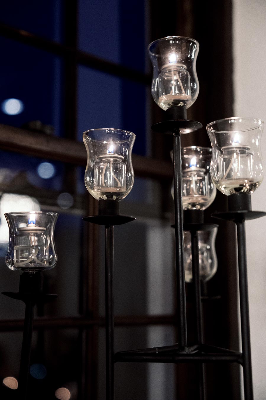 Lit glass candle holders on a black metal stand beside a window at night