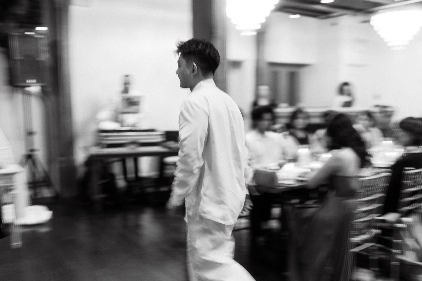 Man in a light suit walking through a blurred indoor reception space
