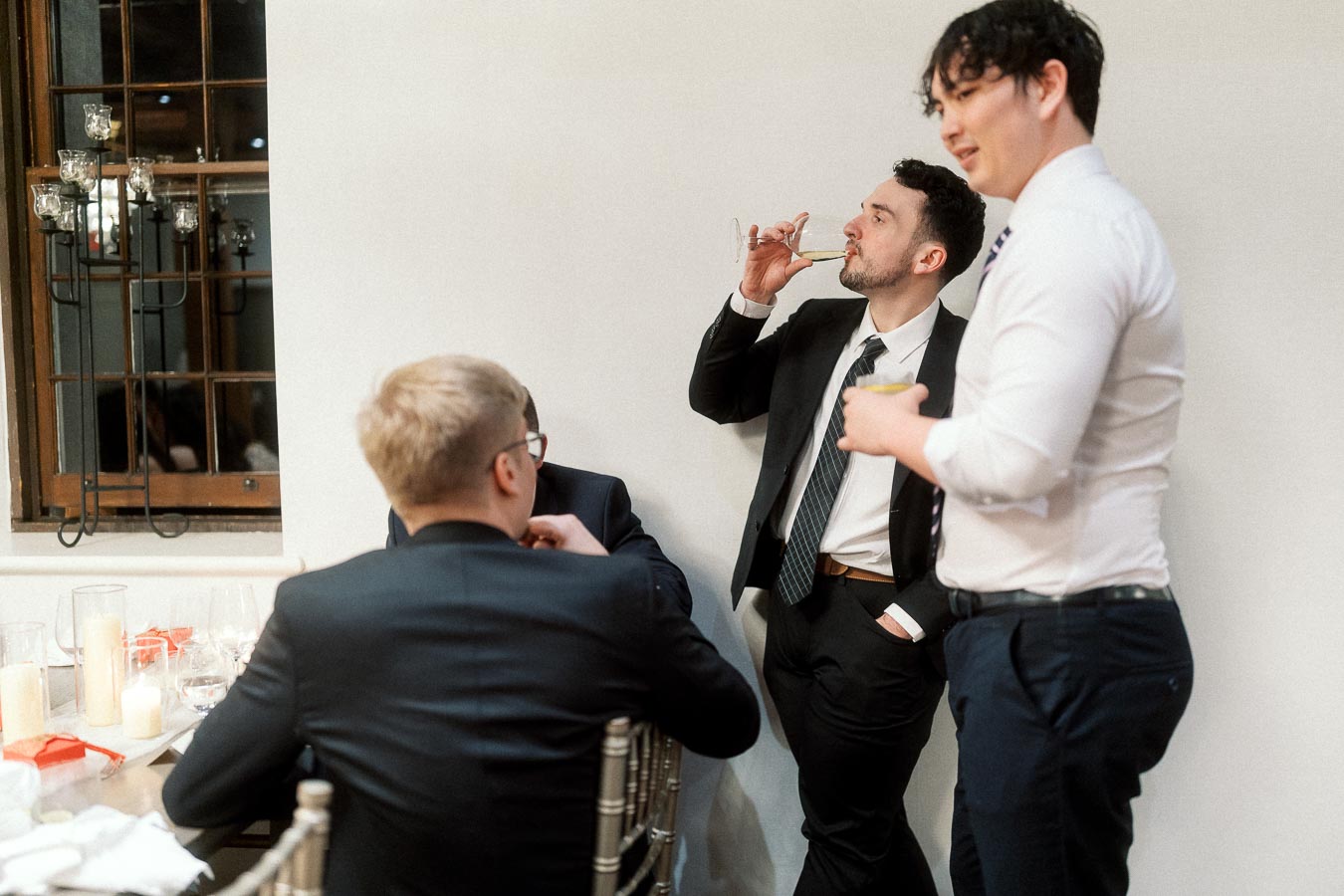 Men in dress shirts and suits chatting with drinks at an indoor celebration