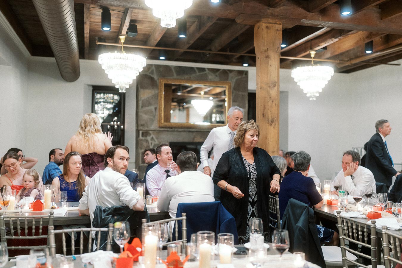 Guests seated at candlelit banquet tables in a rustic reception hall with chandeliers