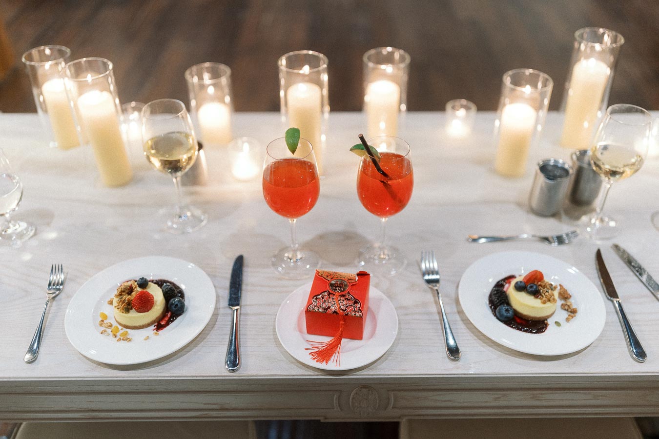 Desserts, red cocktails, wine glasses, candles, and a red gift box on a table