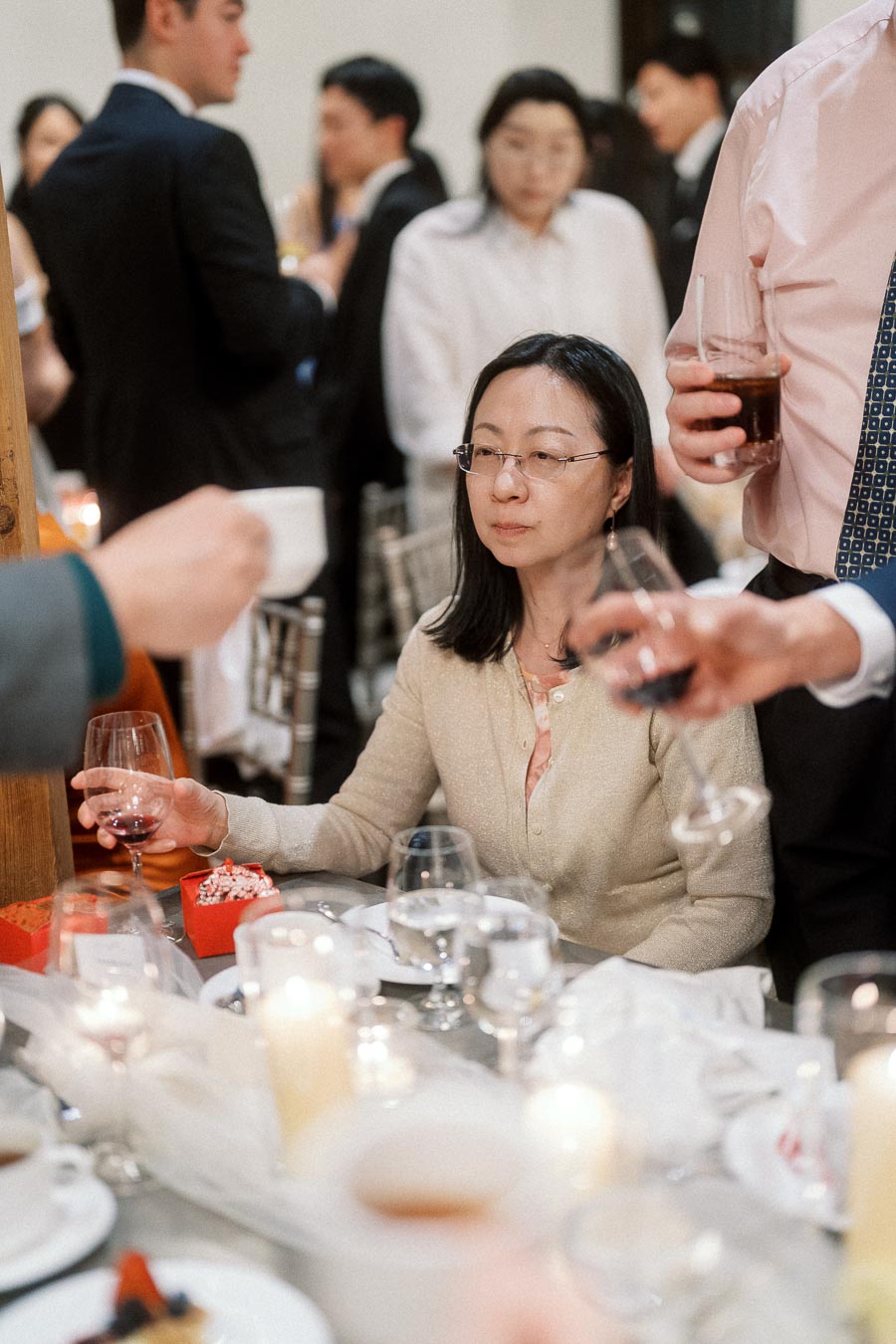 Guest seated at a candlelit dinner table holding wine during a formal celebration
