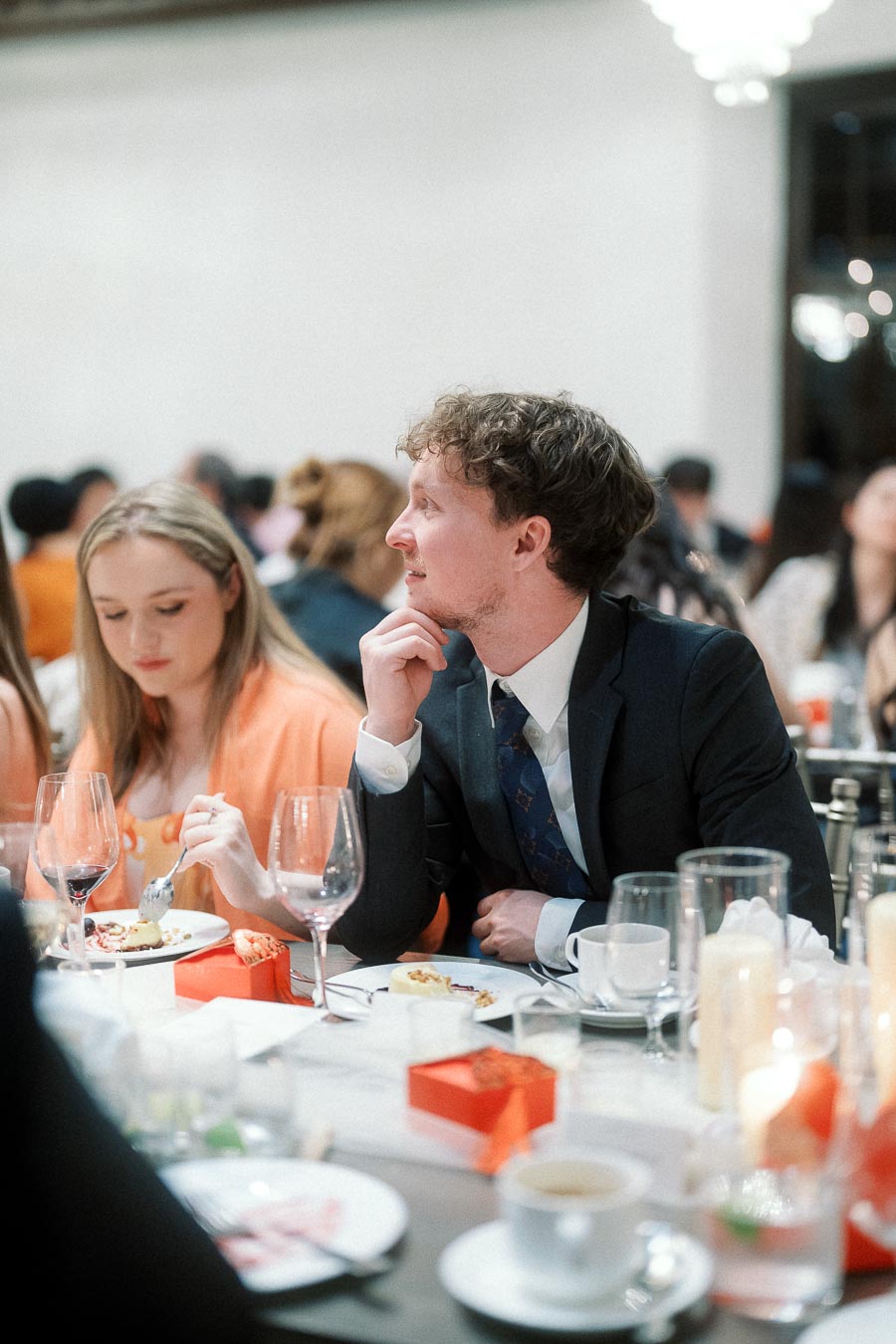 Guests seated at a formal dinner table with wine glasses and plated dessert