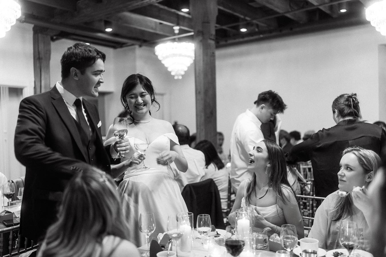 Couple in formal attire smiling with wine glasses during an indoor reception