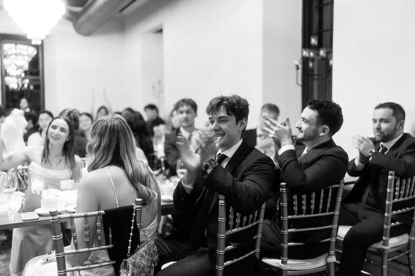 Guests in formal attire applauding at a seated indoor reception