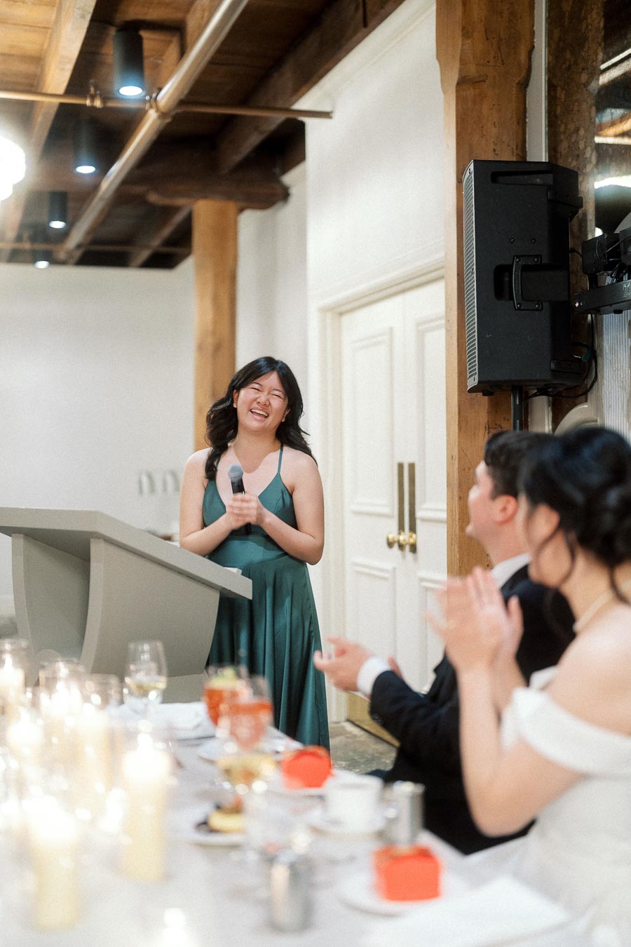 Woman in green dress gives a speech as a seated couple applauds.