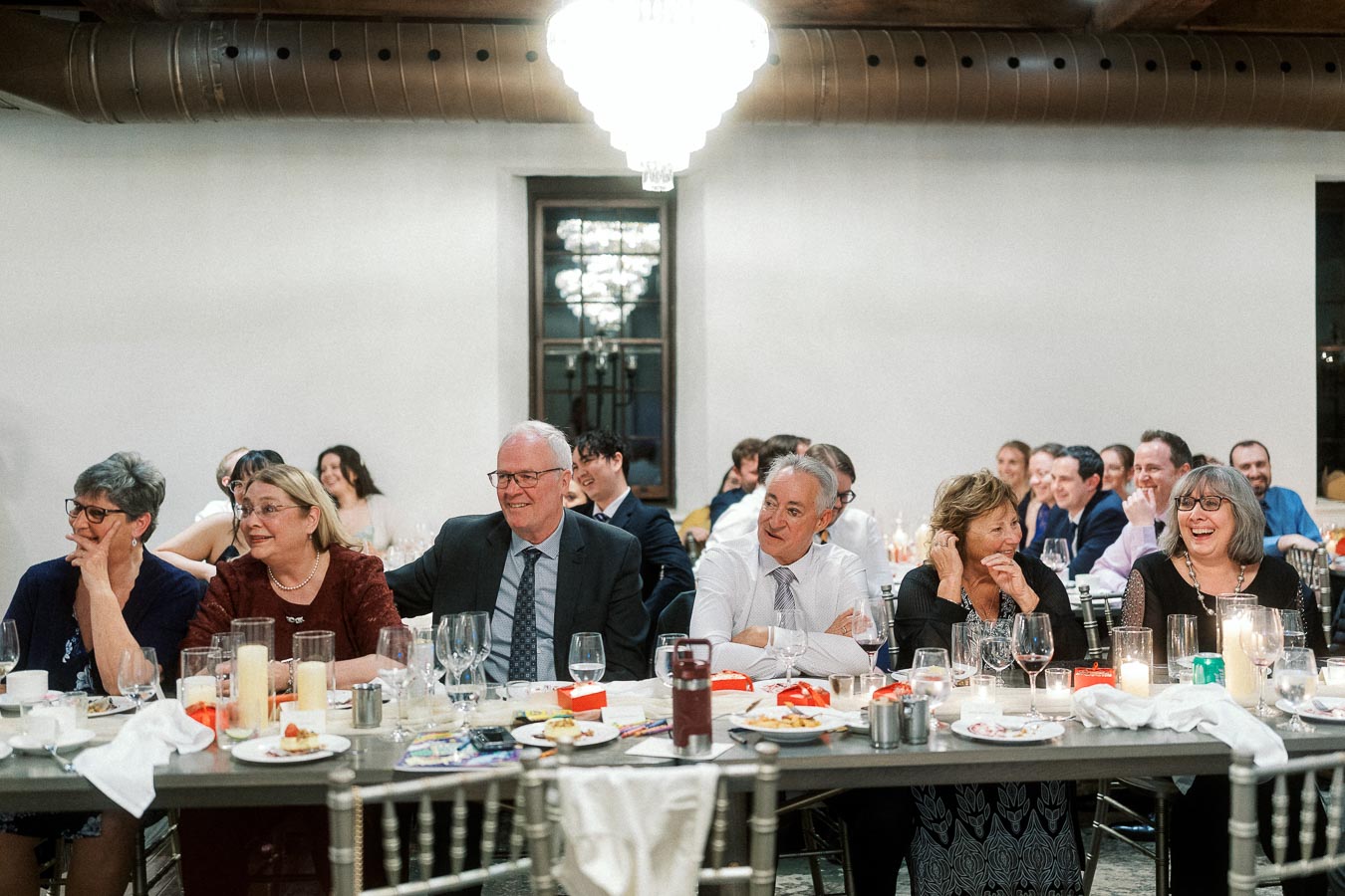 Guests seated at a candlelit banquet table, smiling during a formal indoor celebration.