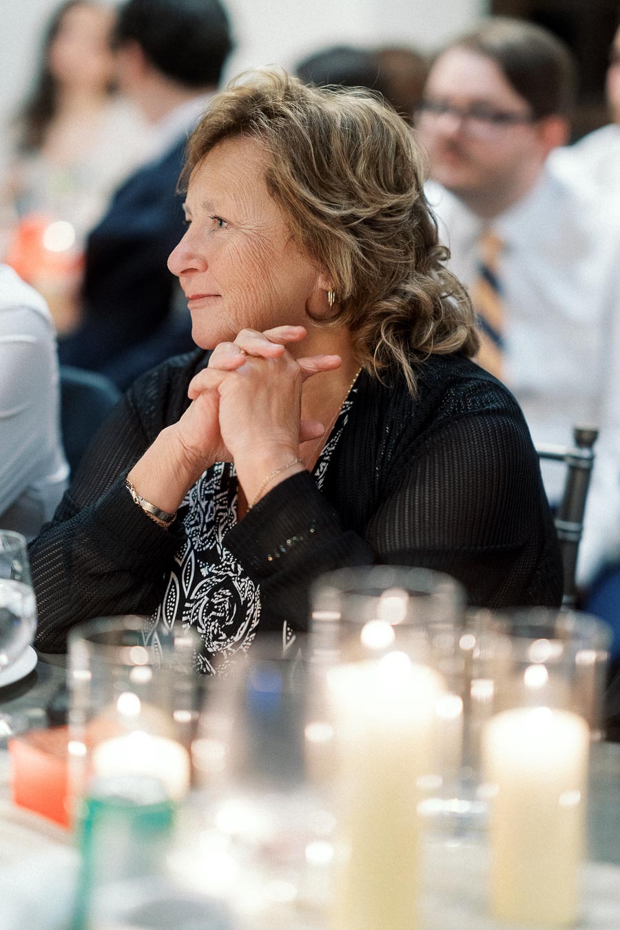 Woman seated at a candlelit table, listening with hands clasped.