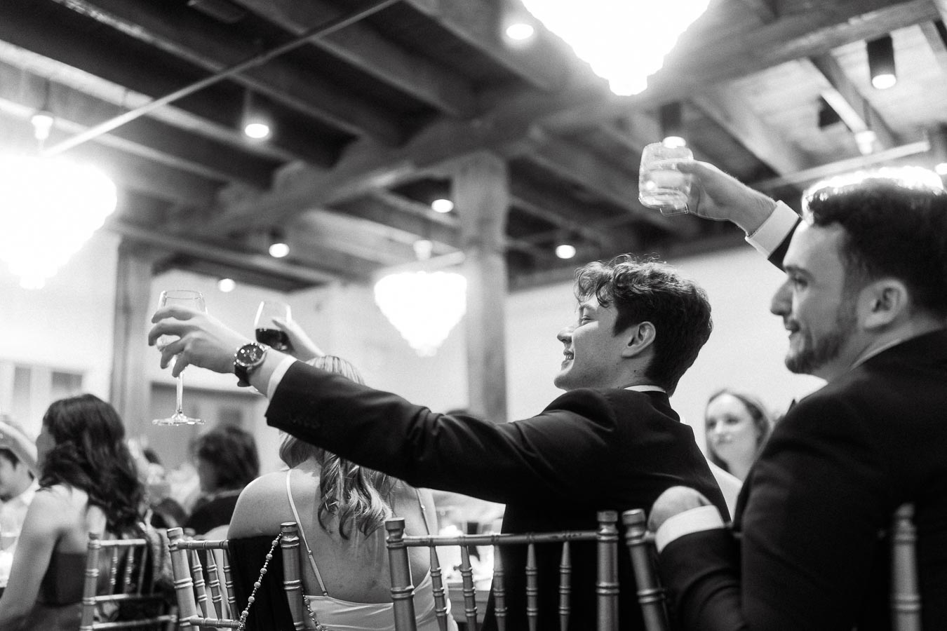 Guests in formalwear raise glasses during a lively indoor celebration.