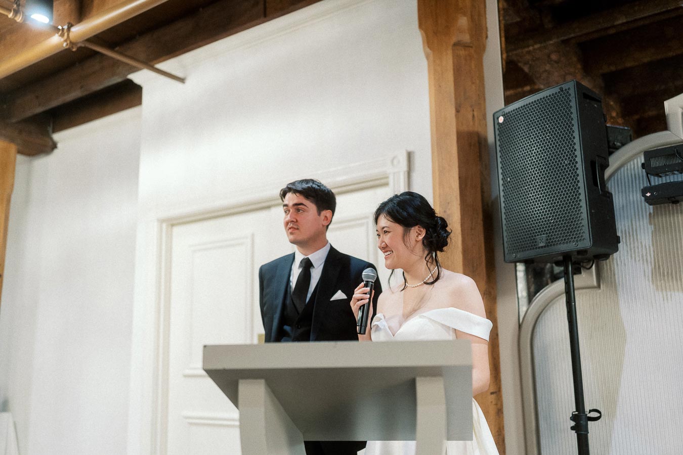 Couple in formal attire standing at a podium, with the woman holding a microphone.