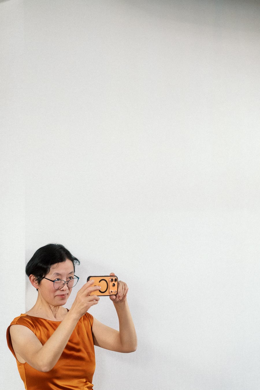 Woman in orange dress holding a phone against a plain wall