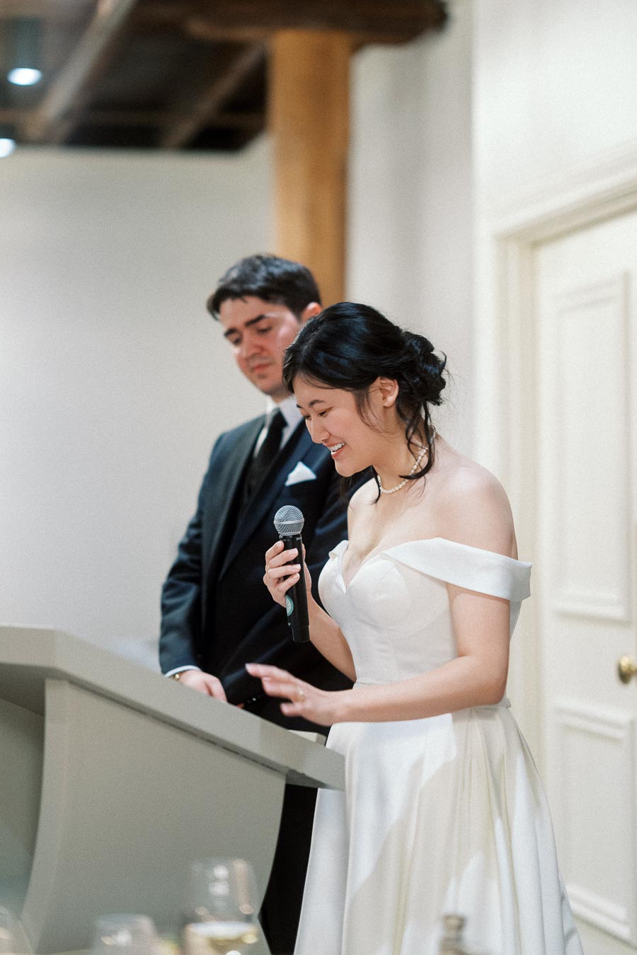 Woman in a white gown speaking into a microphone beside a man in a suit.