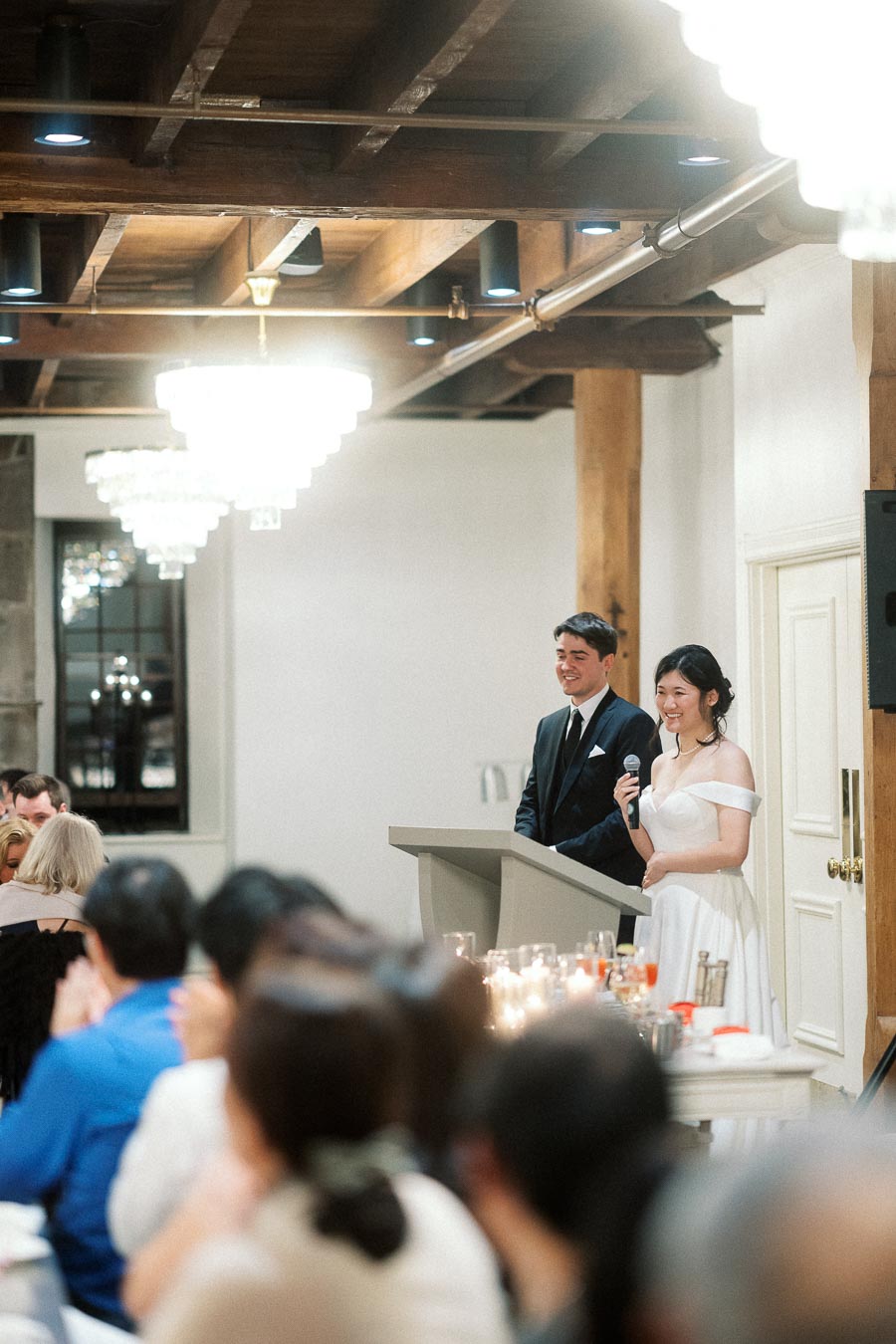 Couple in formal attire speaking at a podium during an indoor reception