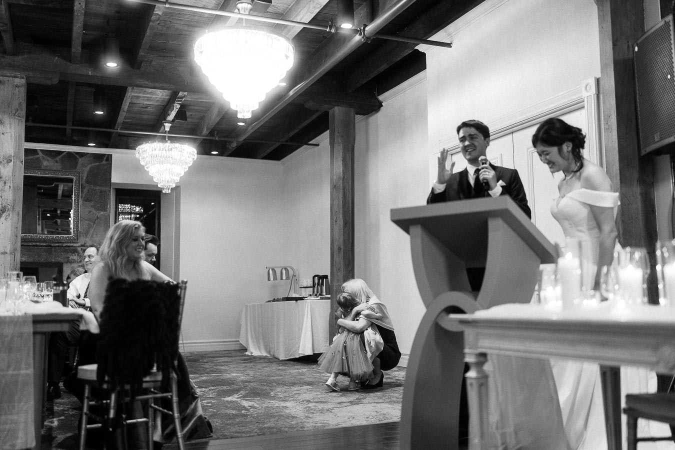 Bride and groom laughing at a podium during an indoor reception speech.