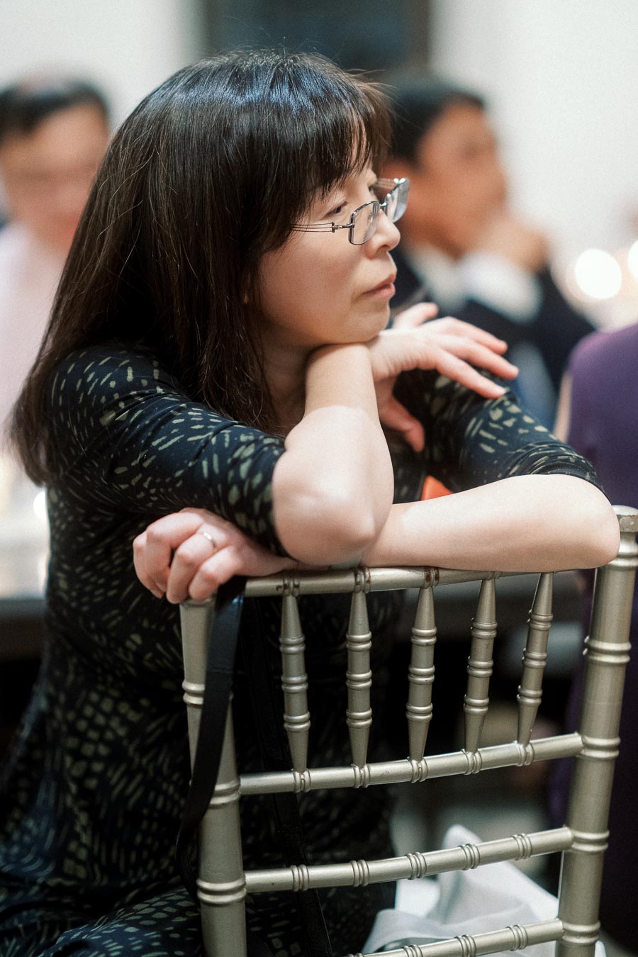 Woman with glasses leaning on a chair during an indoor gathering