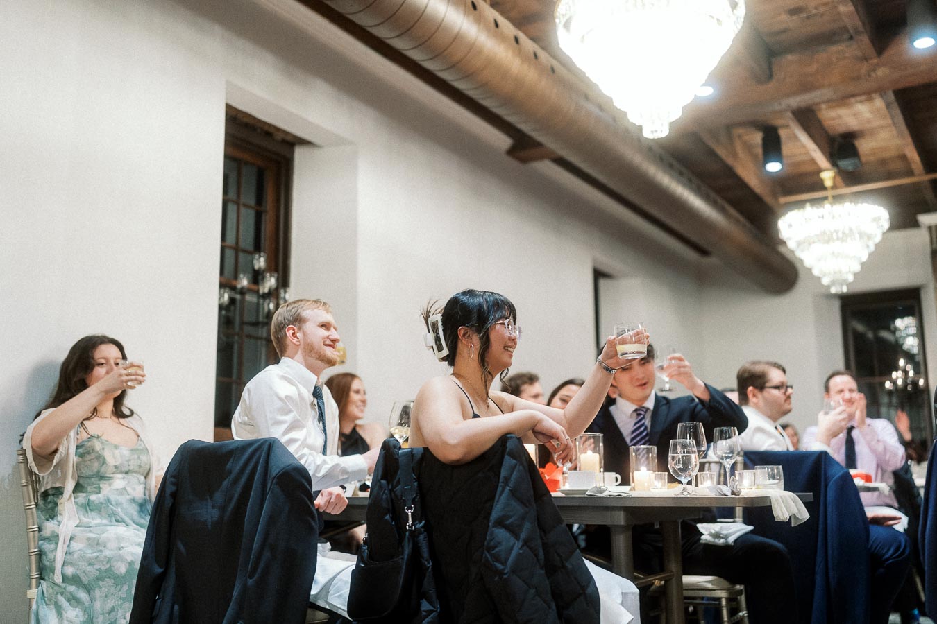 Guests seated indoors raise glasses during a formal dinner toast.