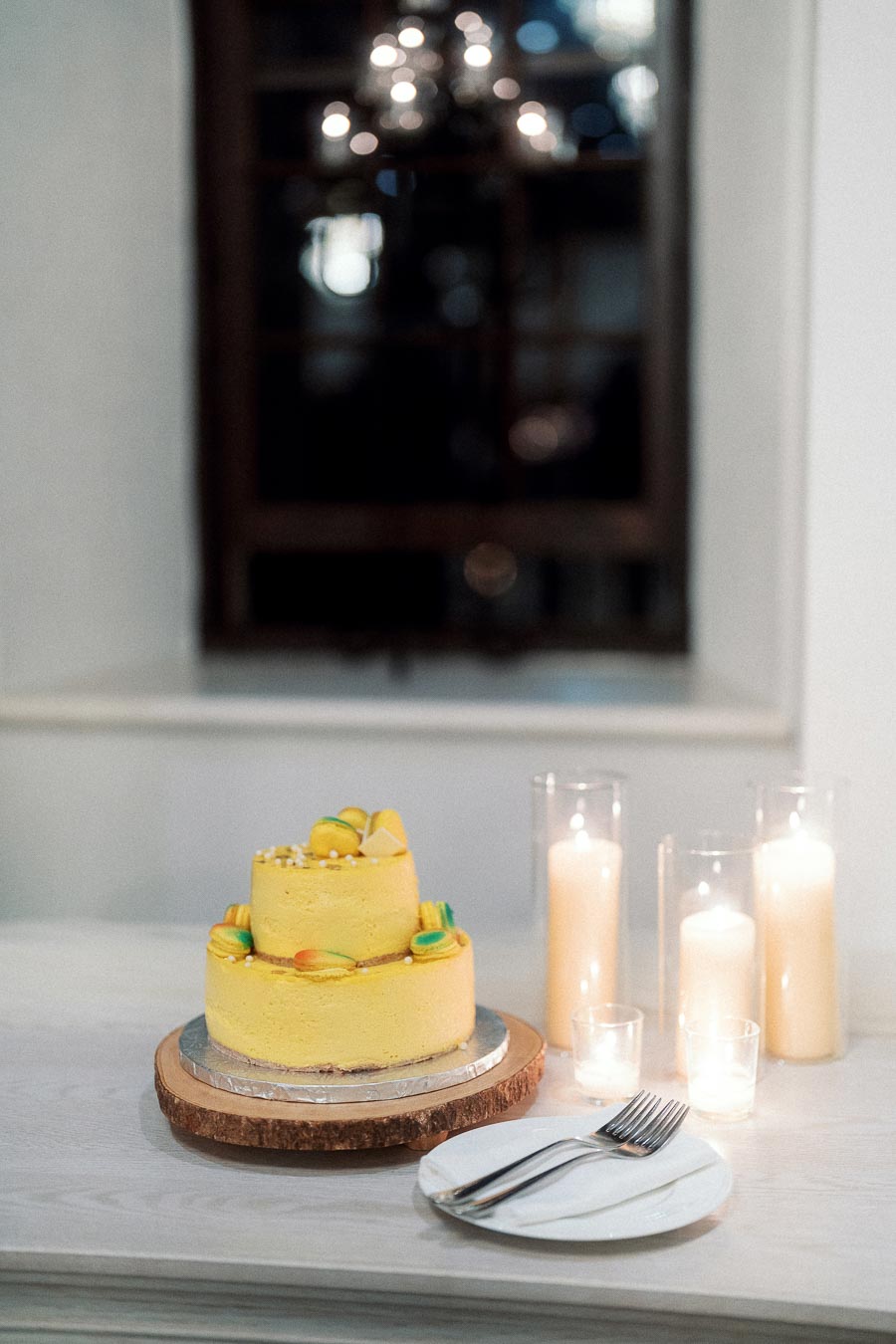 Two-tier yellow cake with candles and plates on a white table