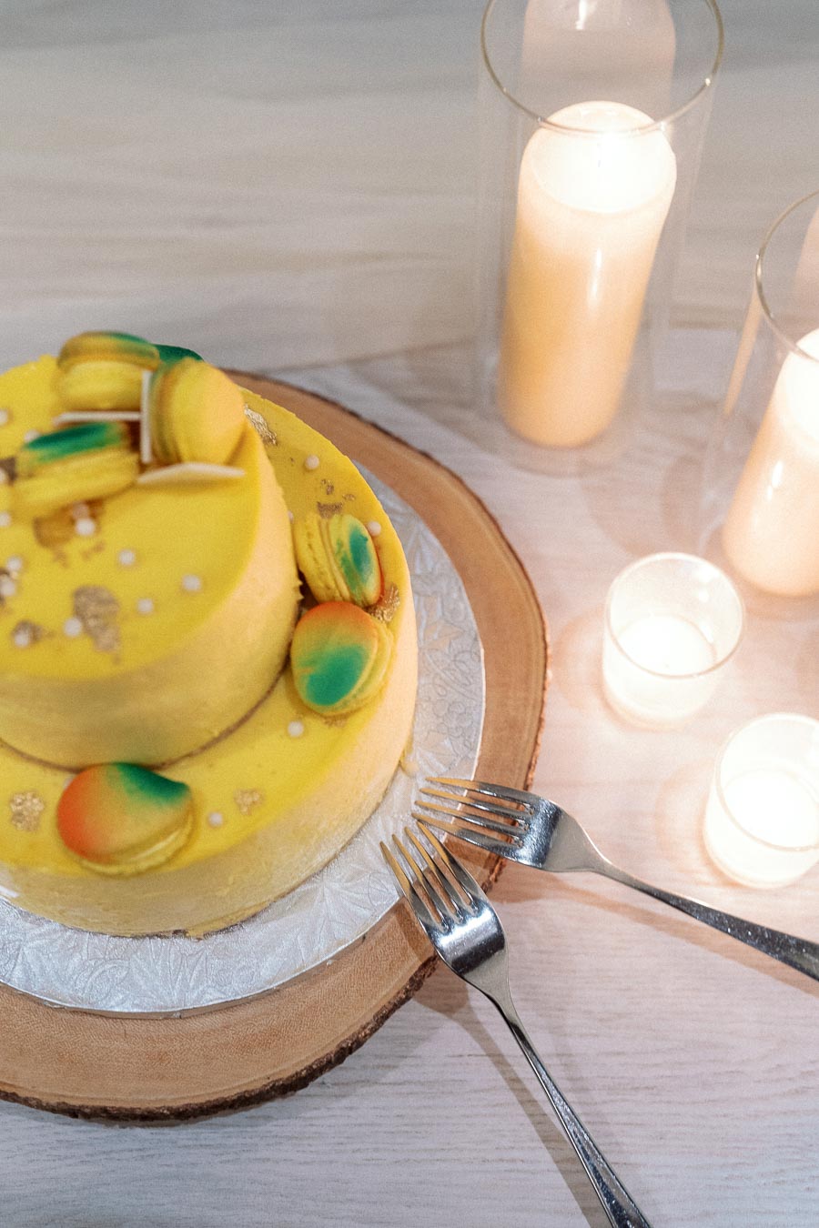 Yellow decorated cake with macarons, forks, and lit candles on a table