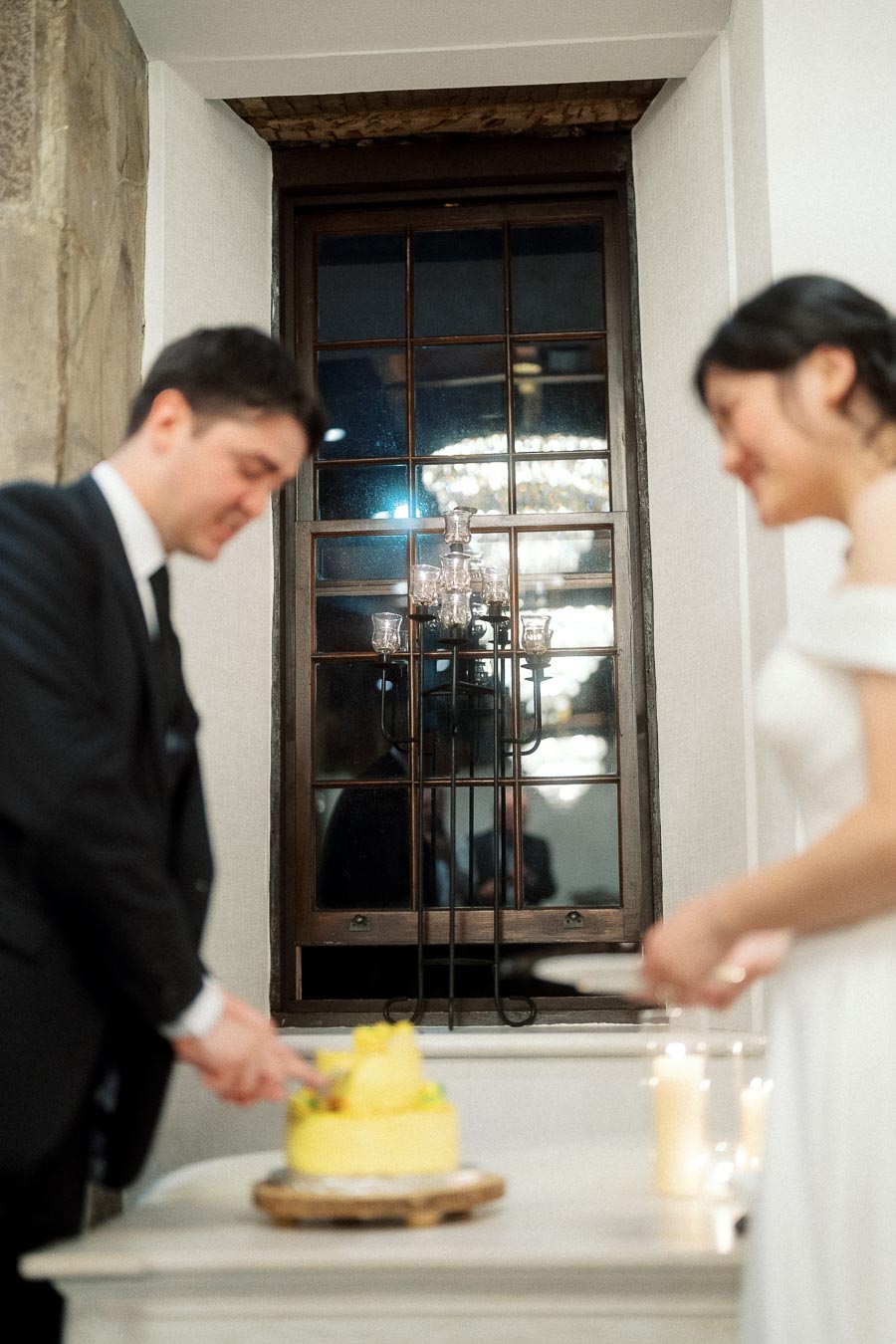 Couple in formal attire cutting a yellow cake beside candles indoors