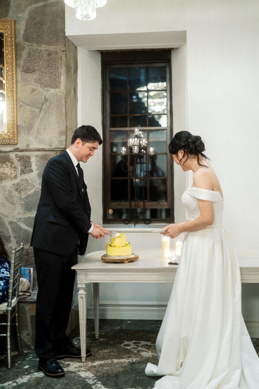 Couple in formal attire cutting a small cake indoors during their engagement photoshoot