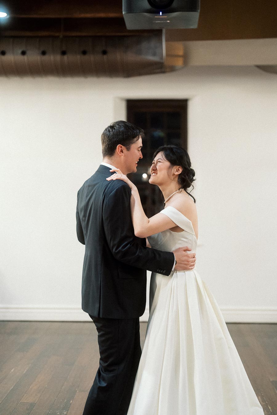 Couple in formal attire laughing together while embracing indoors.