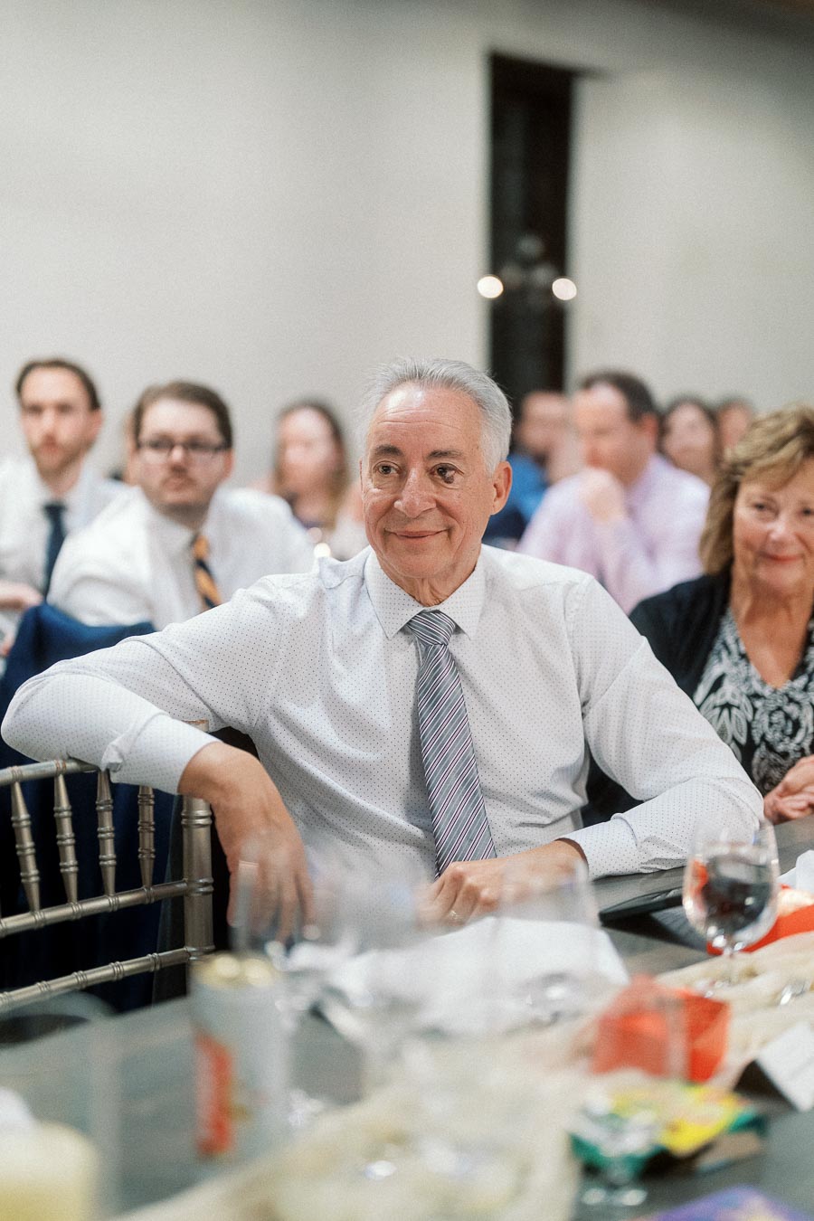 Man in a dress shirt and tie seated among guests at a reception table