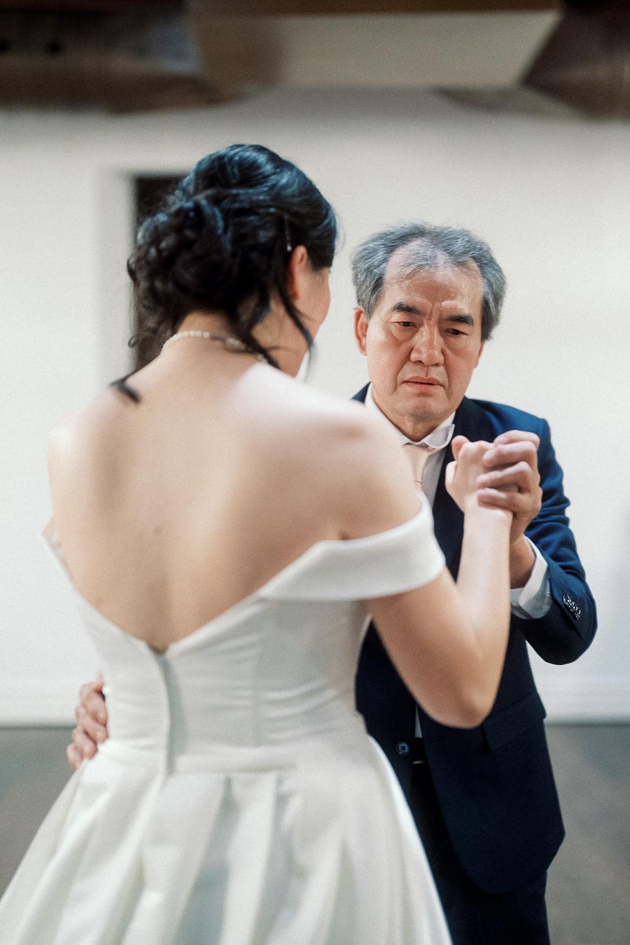 Woman in a white dress dancing with an older man in a suit indoors