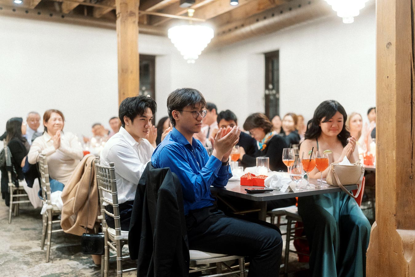 Guests seated at banquet tables applaud during an indoor celebration.