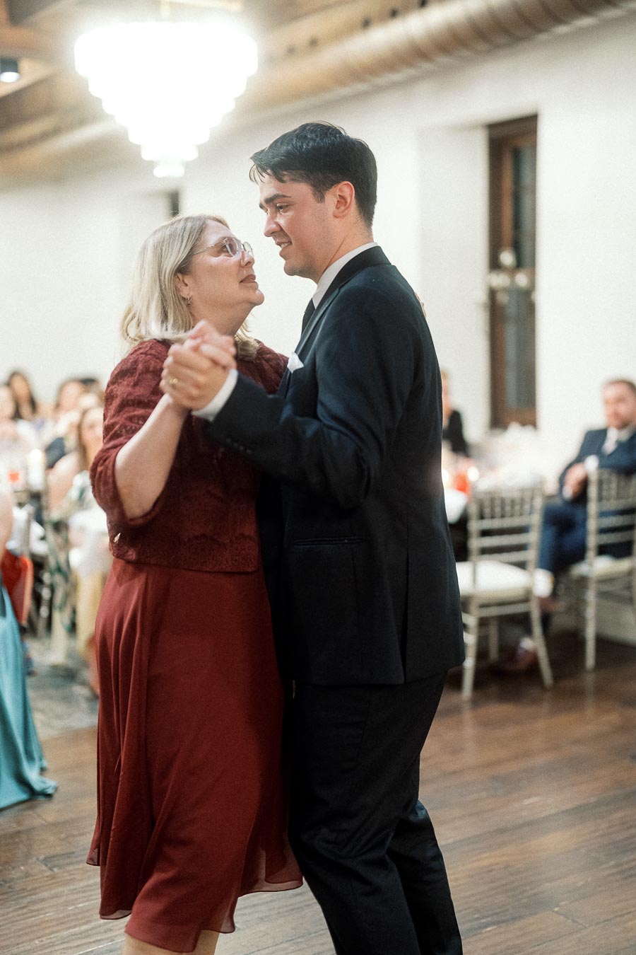 Man in a black suit dances with a woman in a burgundy dress at a reception.