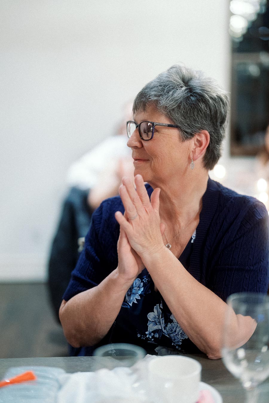 Woman with short gray hair and glasses smiling at a table