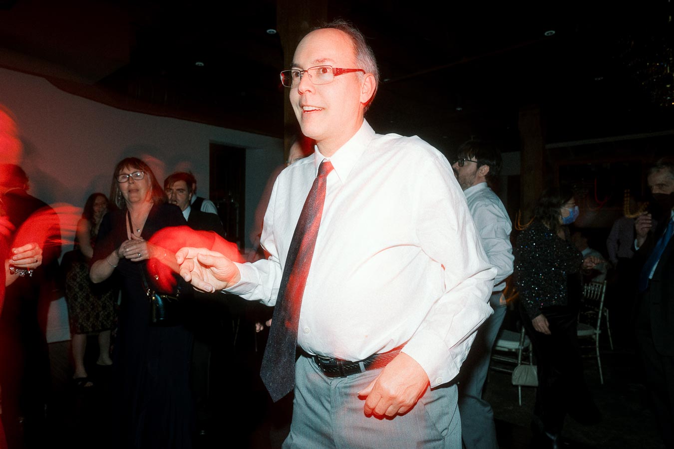Man in a white shirt and tie dancing among guests at an indoor celebration