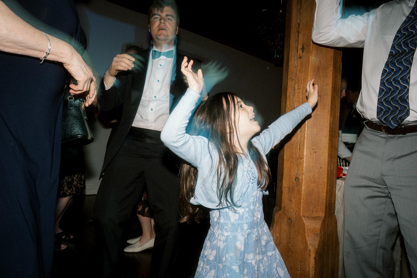 Young girl dancing with raised arms among adults at an indoor celebration.