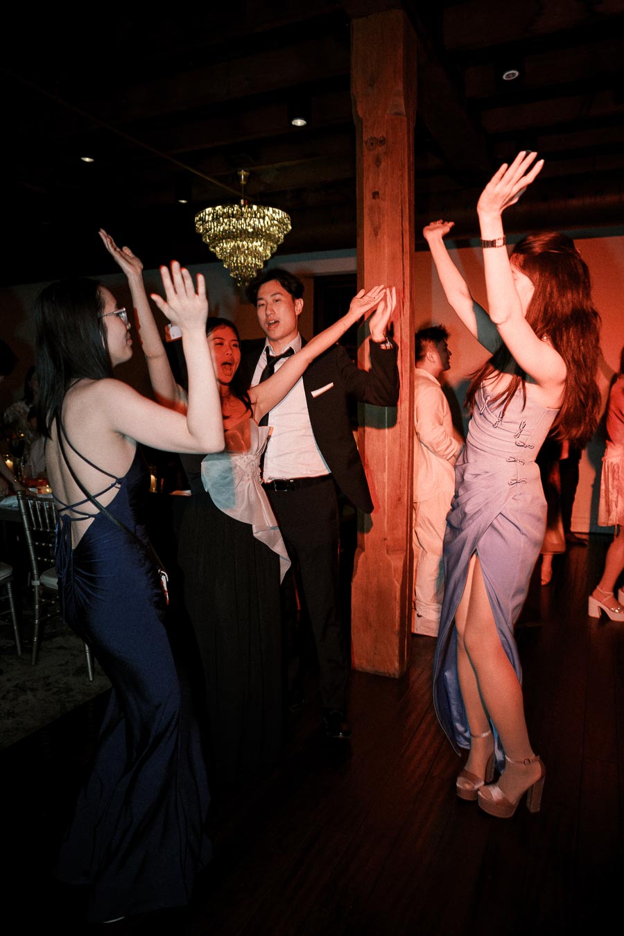 Guests dancing with raised hands on an indoor dance floor under warm party lighting