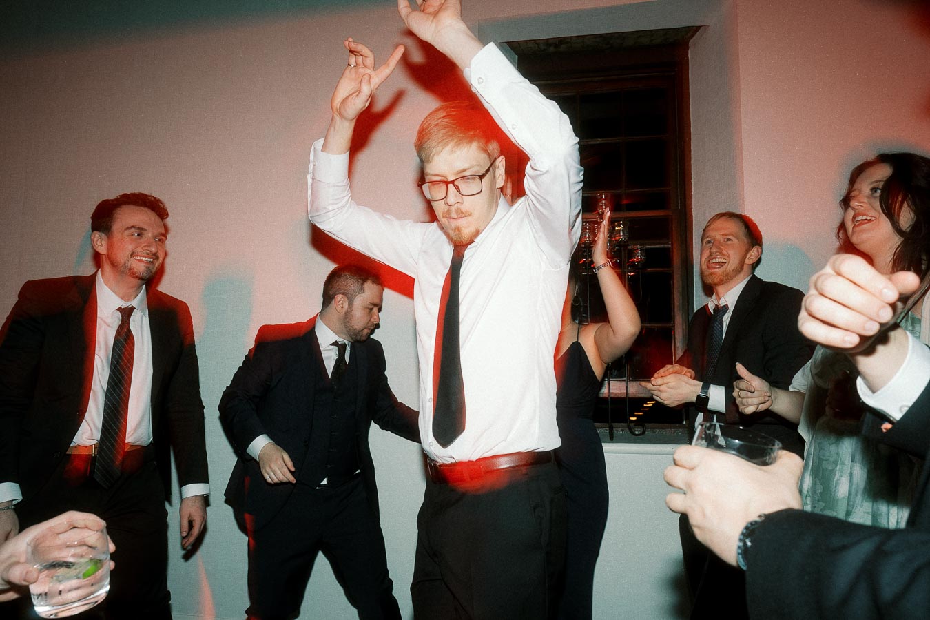 Wedding or engagement party guests dancing indoors with drinks and raised hands
