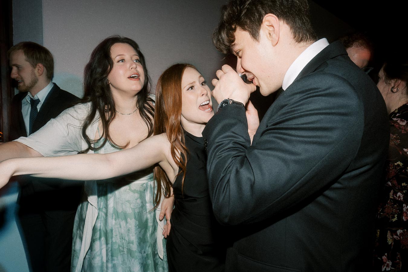 Guests in formalwear dancing and singing together at an indoor celebration