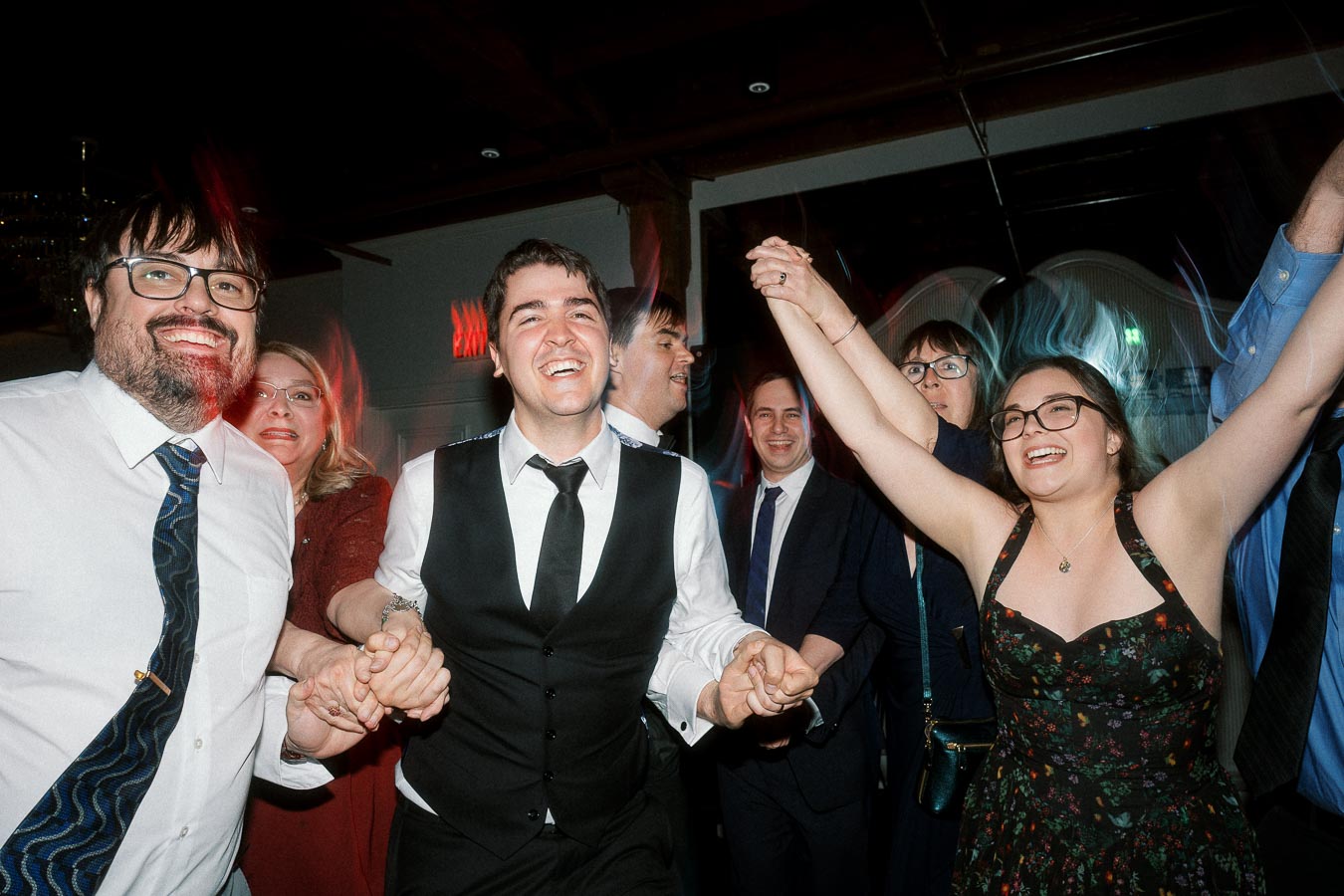 Group of dressed-up guests laughing and holding hands on a lively dance floor