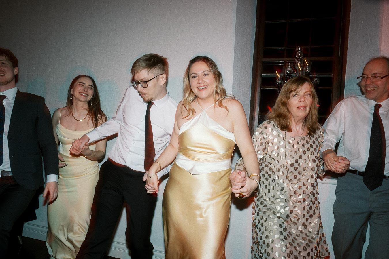 Group of formally dressed people holding hands and dancing indoors.