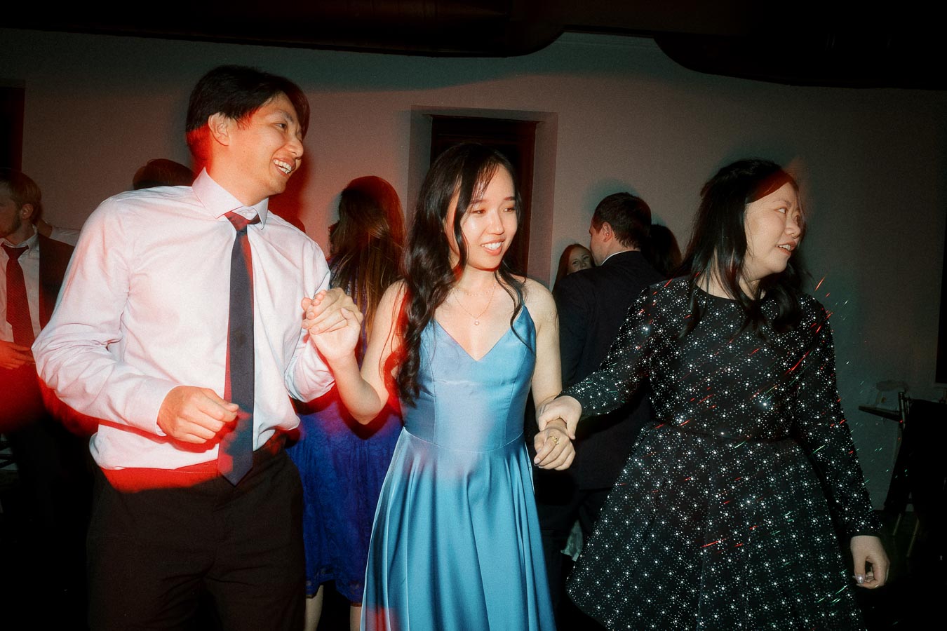 Three guests holding hands and dancing at an indoor celebration.