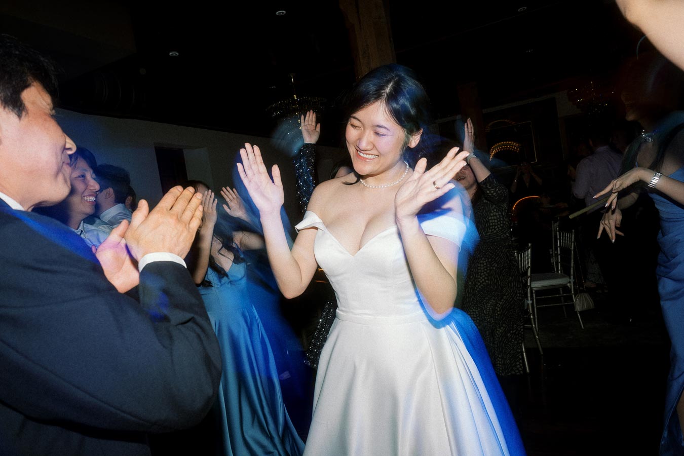 Bride in a white dress dancing with guests at a dimly lit reception
