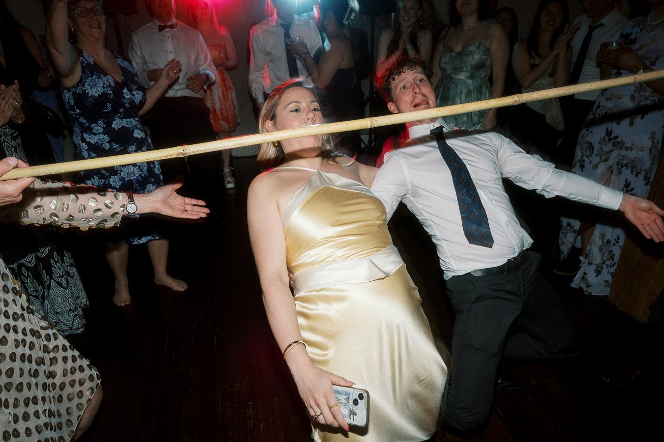 Couple leaning back under a limbo stick on a crowded dance floor