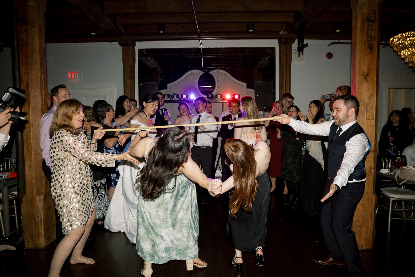 Wedding guests laughing and dancing during a limbo game at a reception
