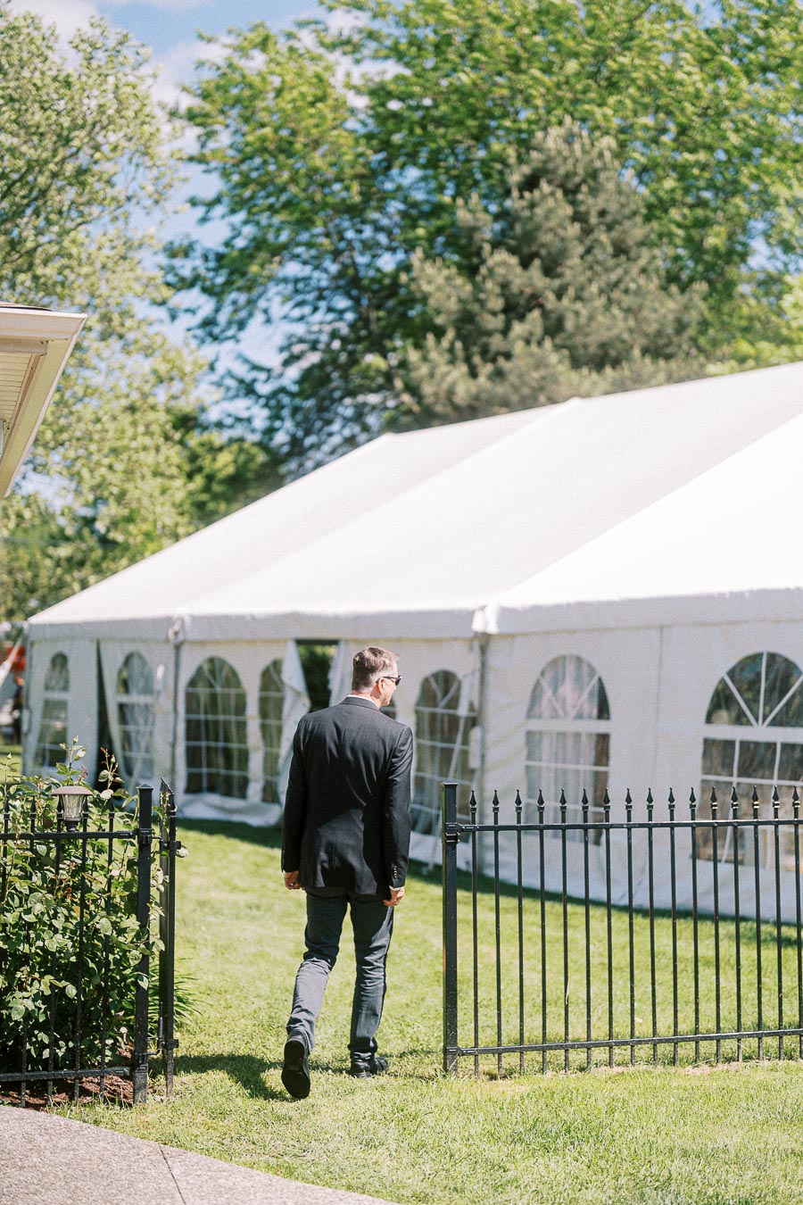 Man in formal attire walking towards a large outdoor white tent on a sunny day.