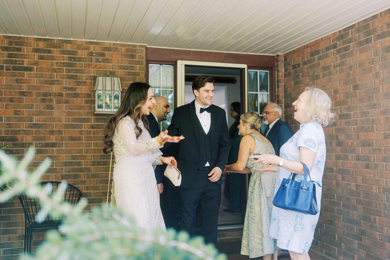 Group of people in formal attire sharing a joyful moment at the entrance of a brick building, highlighting social interactions at a sophisticated event.