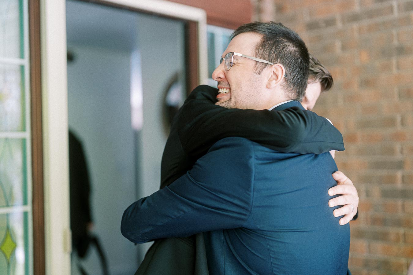 Two men in formal wear embracing in a warm hug, capturing a moment of friendship and celebration indoors.