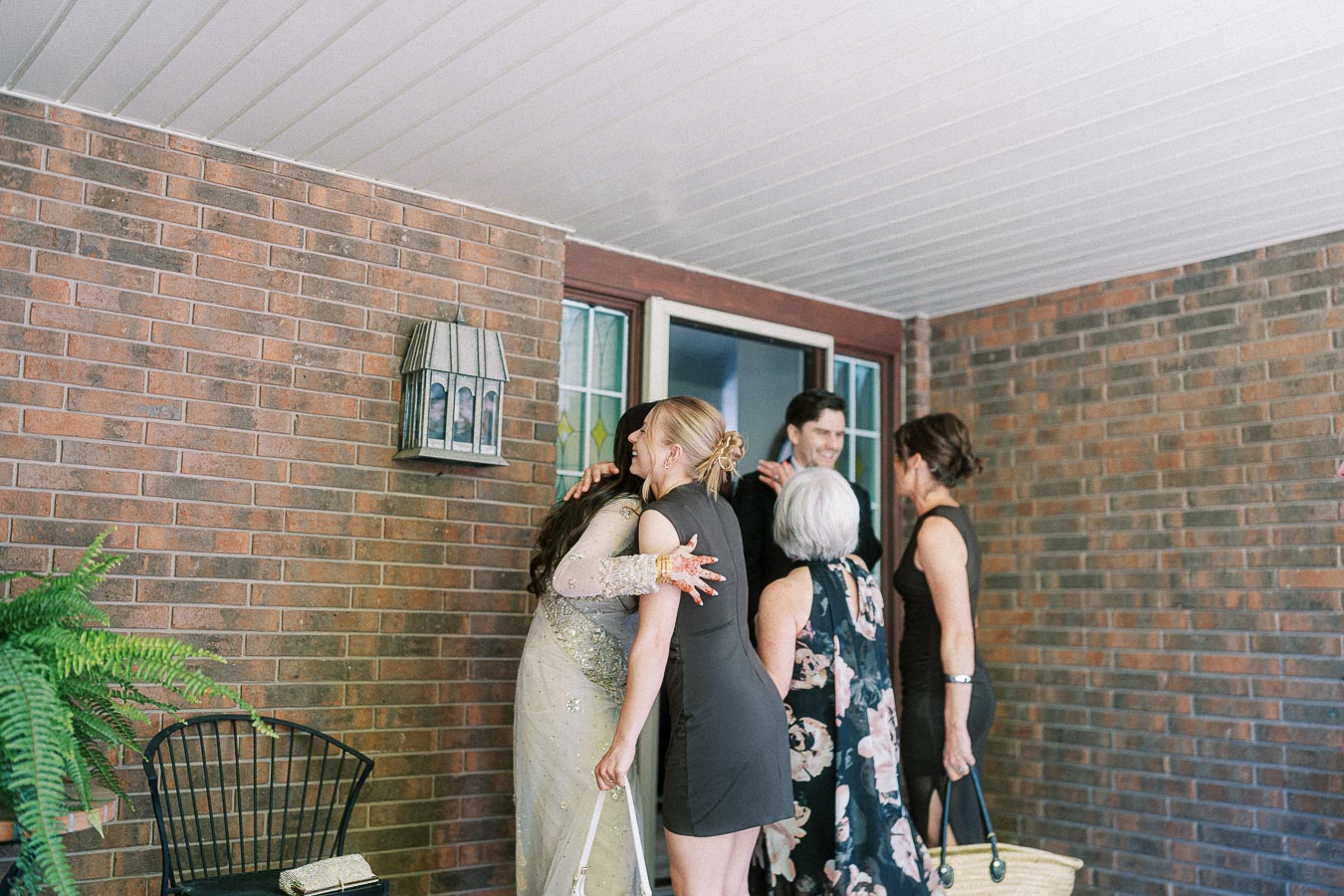 Group of people warmly greeting each other on a brick house porch.