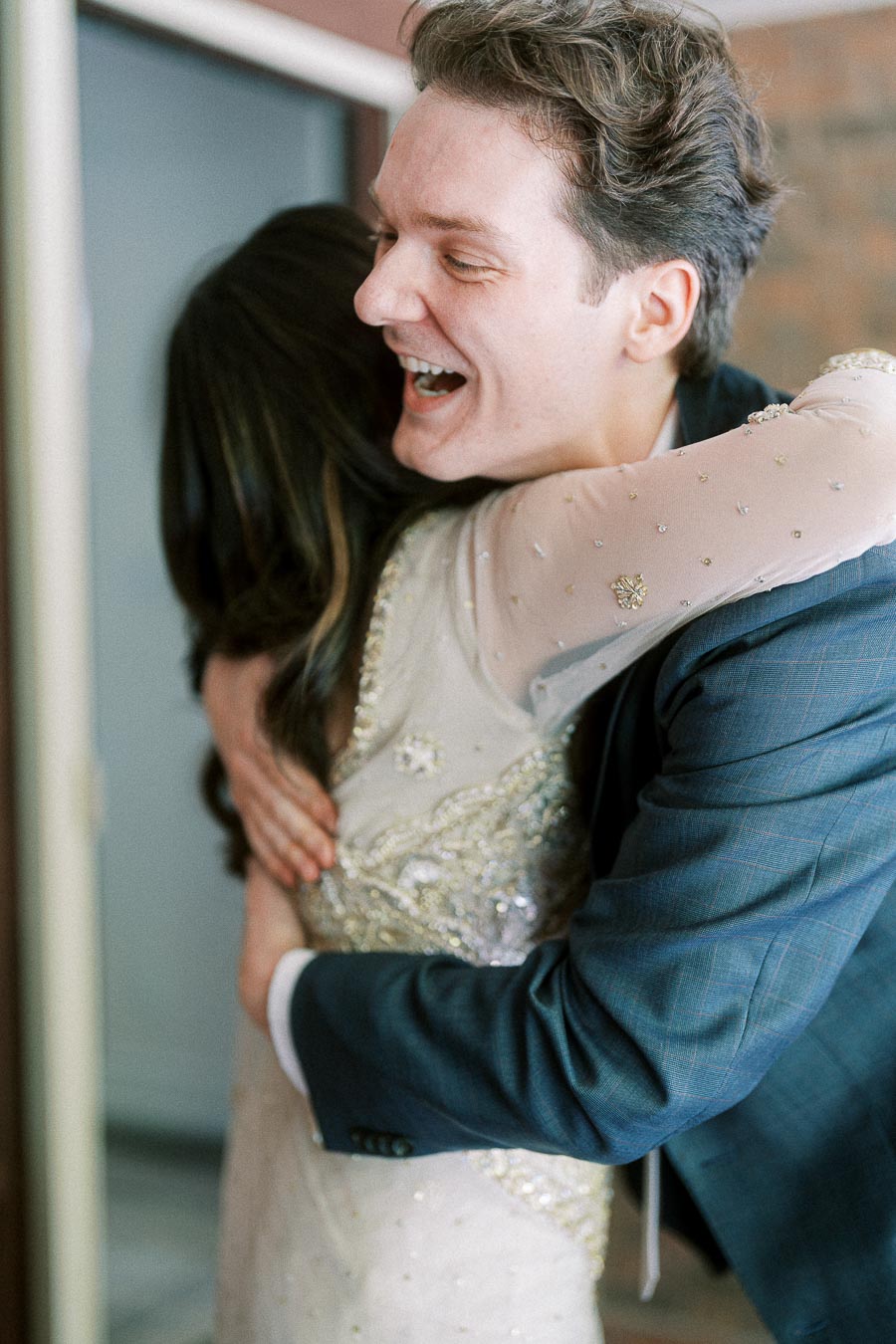 Joyful embrace between a man in a blue suit and a woman in an elegant dress, expressing happiness and celebration.